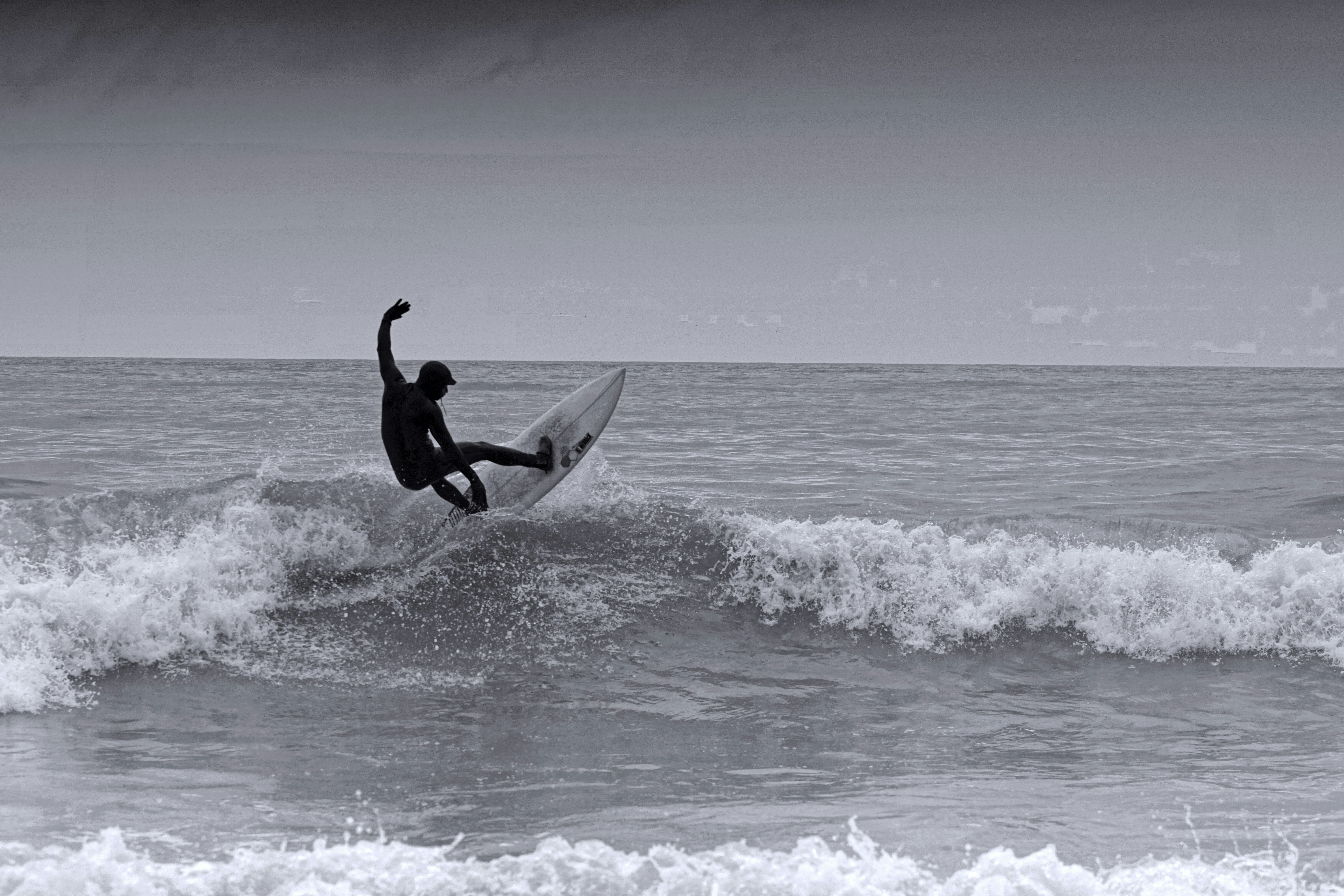 grayscale photo of man surfing on sea waves