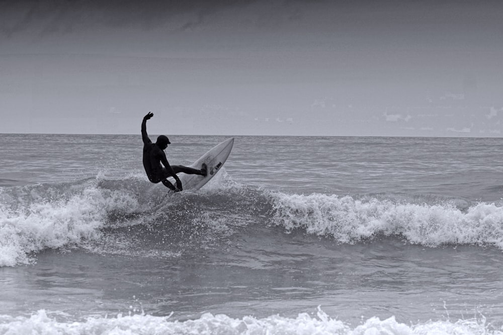 海の波でサーフィンする男のグレースケール写真