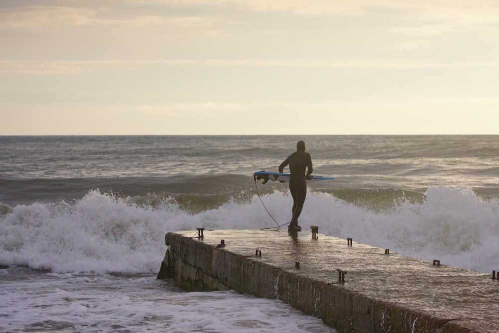 man in black tank top and black shorts holding a white surfboard on a beach during