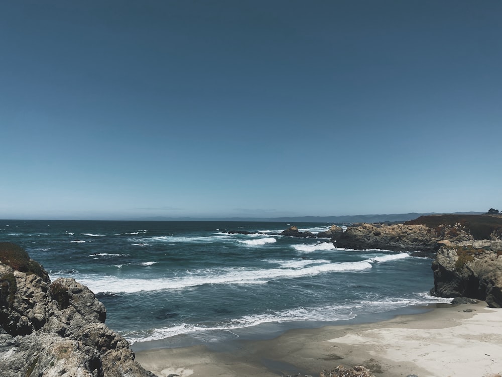 ocean waves crashing on rocks under blue sky during daytime