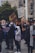 A diverse group of people gather outdoors, many wearing face masks. They hold signs with messages advocating for racial justice and social change, including 'Black Lives Matter' and 'Silence is Violence.' The setting is urban, with modern architecture and greenery in the background.