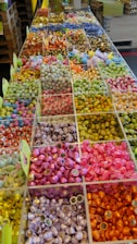 An arrangement of various colorful candies is displayed in clear compartments, creating a mosaic of vibrant hues. Each section is filled with neatly organized sweets, varying in size, shape, and color, including shiny wrappers and different textures.