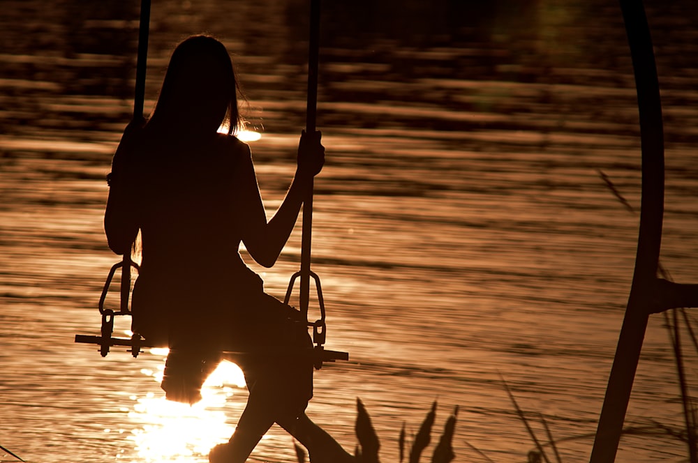 silhouette of woman sitting on swing during sunset