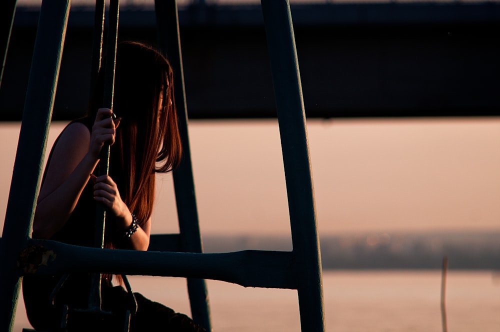 femme en débardeur noir debout à côté de balustrades en métal noir au coucher du soleil