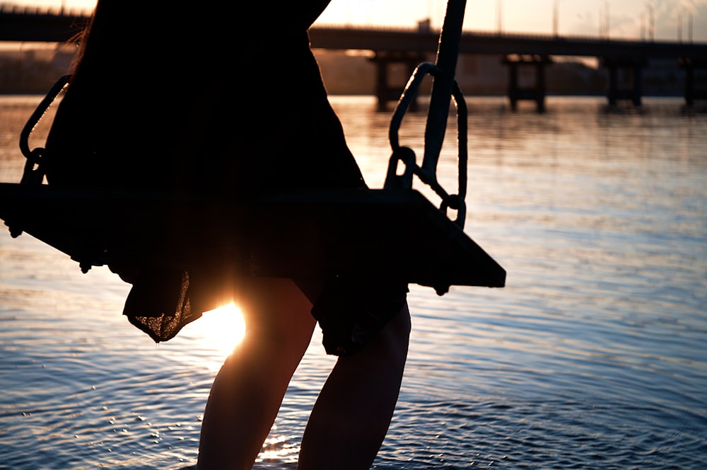 person sitting on swing near body of water during sunset