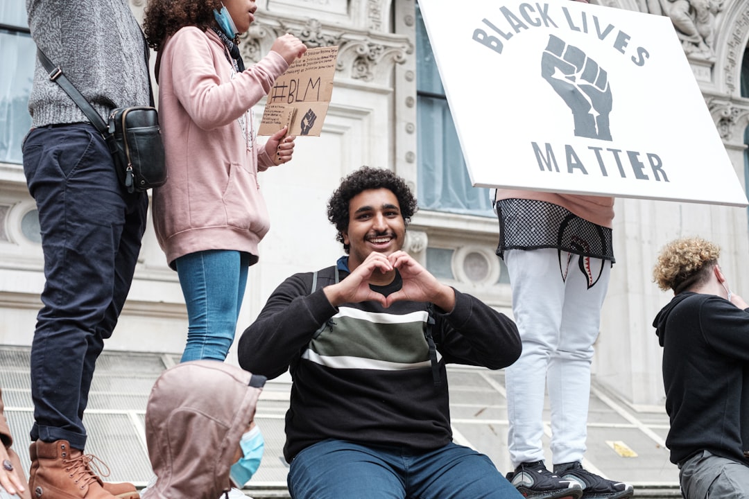 woman in black and white long sleeve shirt and blue denim jeans holding smartphone, London Black Lives Matter Peaceful P