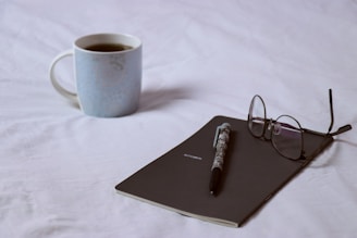blue ceramic mug beside black framed eyeglasses on white table