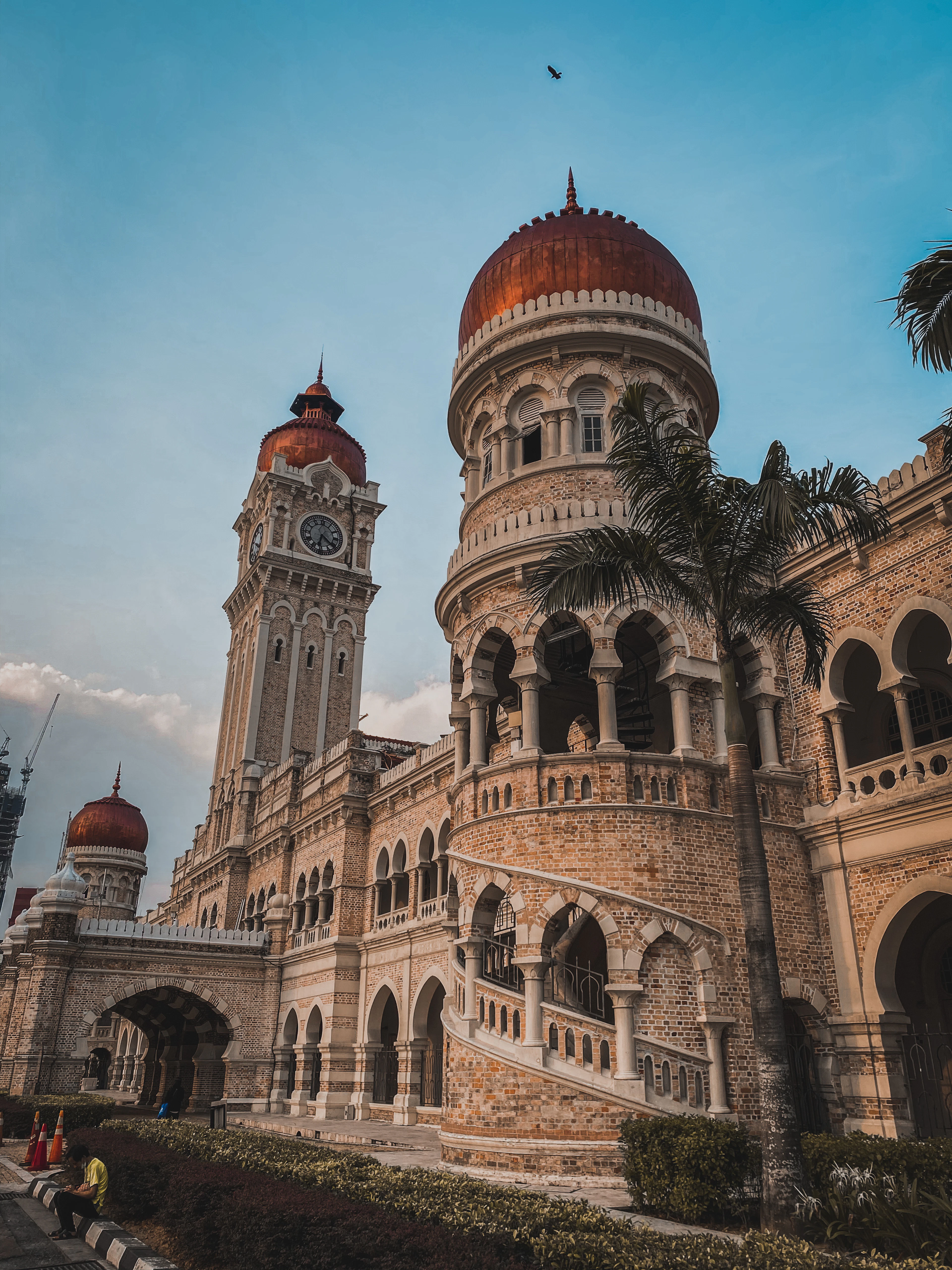 The Moorish arches, copper domes and clock tower of the Sultan Abdul Samad Building on Merdeka Square in Kuala Lumpur, warm sandstone against a deep blue sky.