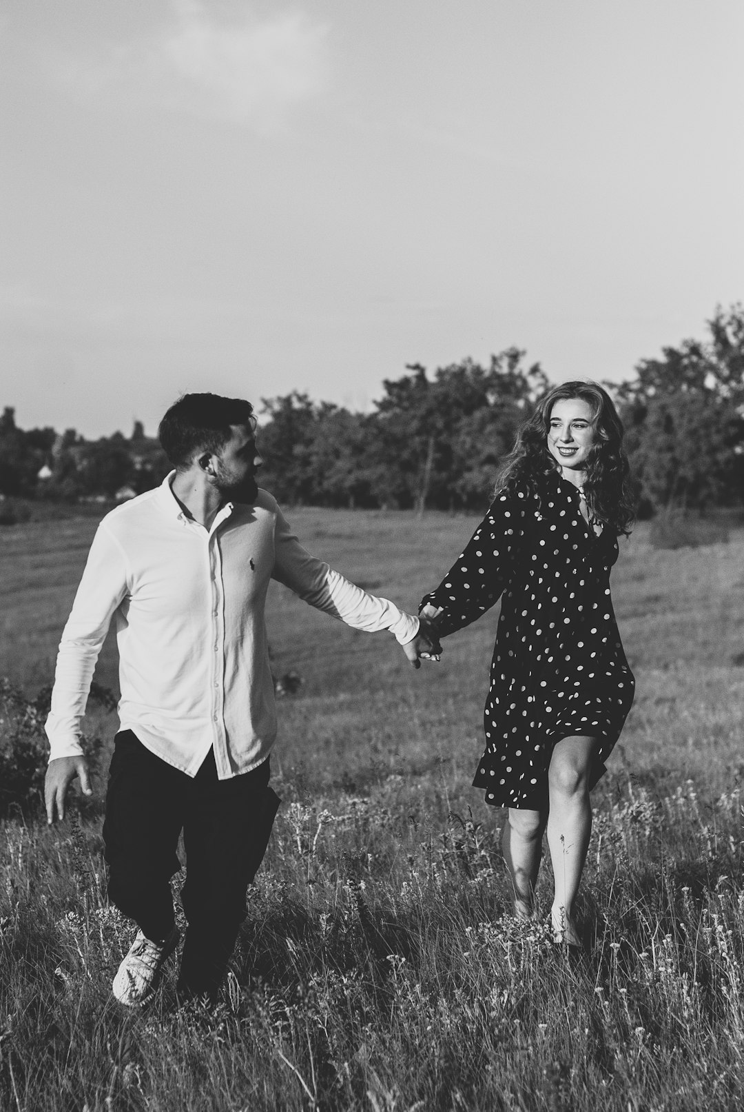 man and woman holding hands on grass field in grayscale photography