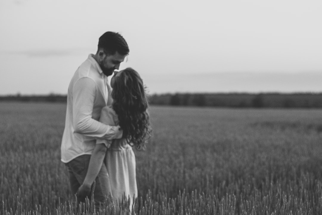 man and woman kissing on grass field in grayscale photography