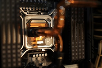 A close-up view of a computer's internal components, highlighting a water cooling block with a metallic frame and transparent section showing fluid. Nearby are RAM sticks installed on the motherboard along with various electronic components.