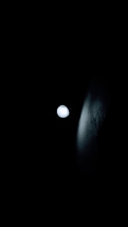 A single bright light source illuminates against a dark backdrop, casting subtle shadows and highlights on a nearby textured surface.