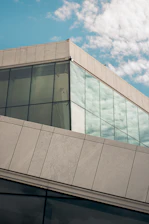 A modern university building with large glass windows reflecting the blue sky.