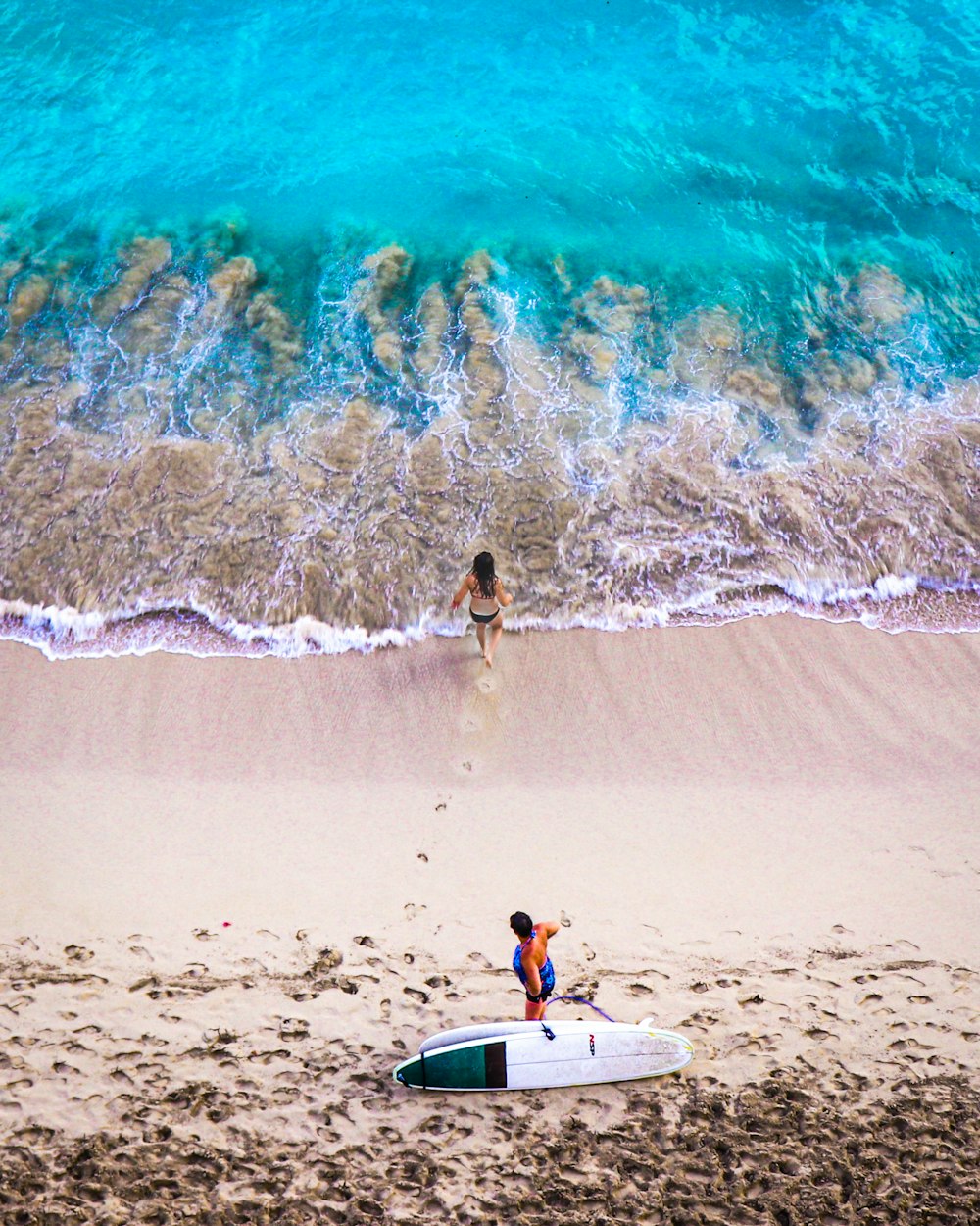 a couple of people standing on top of a beach next to a surfboard