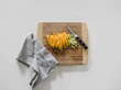 Hand holding a bamboo cutting board next to a set of sharp knives and fresh vegetables on a clean countertop.