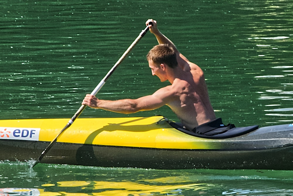 uomo in pantaloncini neri che cavalca kayak giallo sull'acqua verde durante il giorno