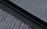 An e-reader device displaying a page of text is partially visible, resting on a textured fabric surface. The focus is on the edge of the device, highlighting its black frame and digital screen with gray text.