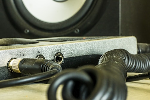A close-up view of audio equipment featuring multiple cables and input jacks. The focus is on a panel with several labeled input slots, including a headphone jack and inputs labeled IN3 and IN4. The equipment is surrounded by coiled black cables, suggesting it's part of a studio or sound system setup.