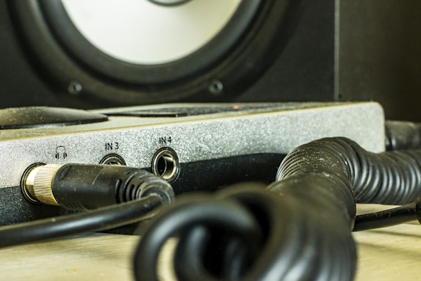 A close-up view of audio equipment featuring multiple cables and input jacks. The focus is on a panel with several labeled input slots, including a headphone jack and inputs labeled IN3 and IN4. The equipment is surrounded by coiled black cables, suggesting it's part of a studio or sound system setup.