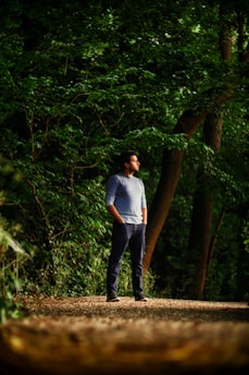 A person standing at a forked path in a forest, looking thoughtfully toward multiple directions.