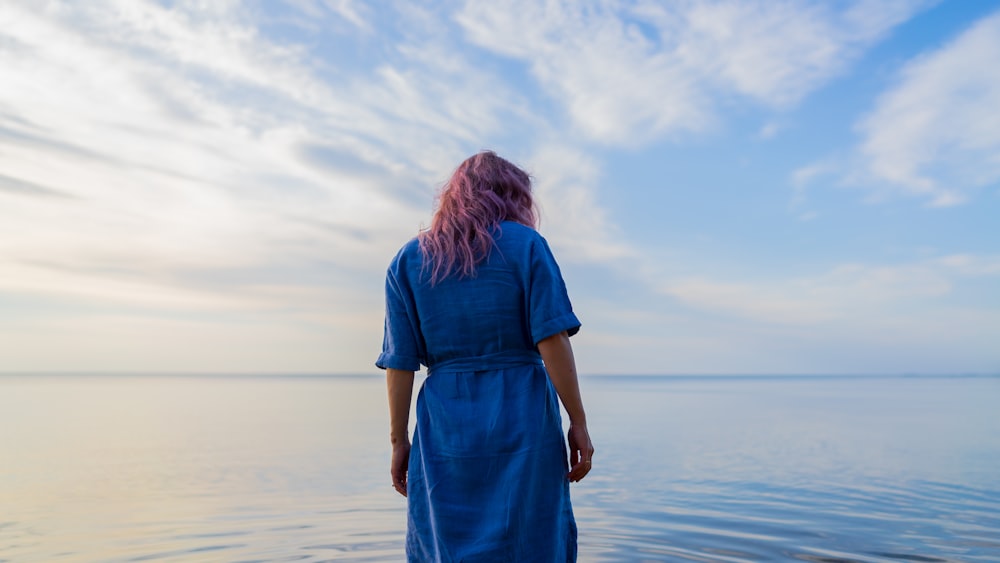 donna in vestito blu in piedi sulla spiaggia durante il giorno