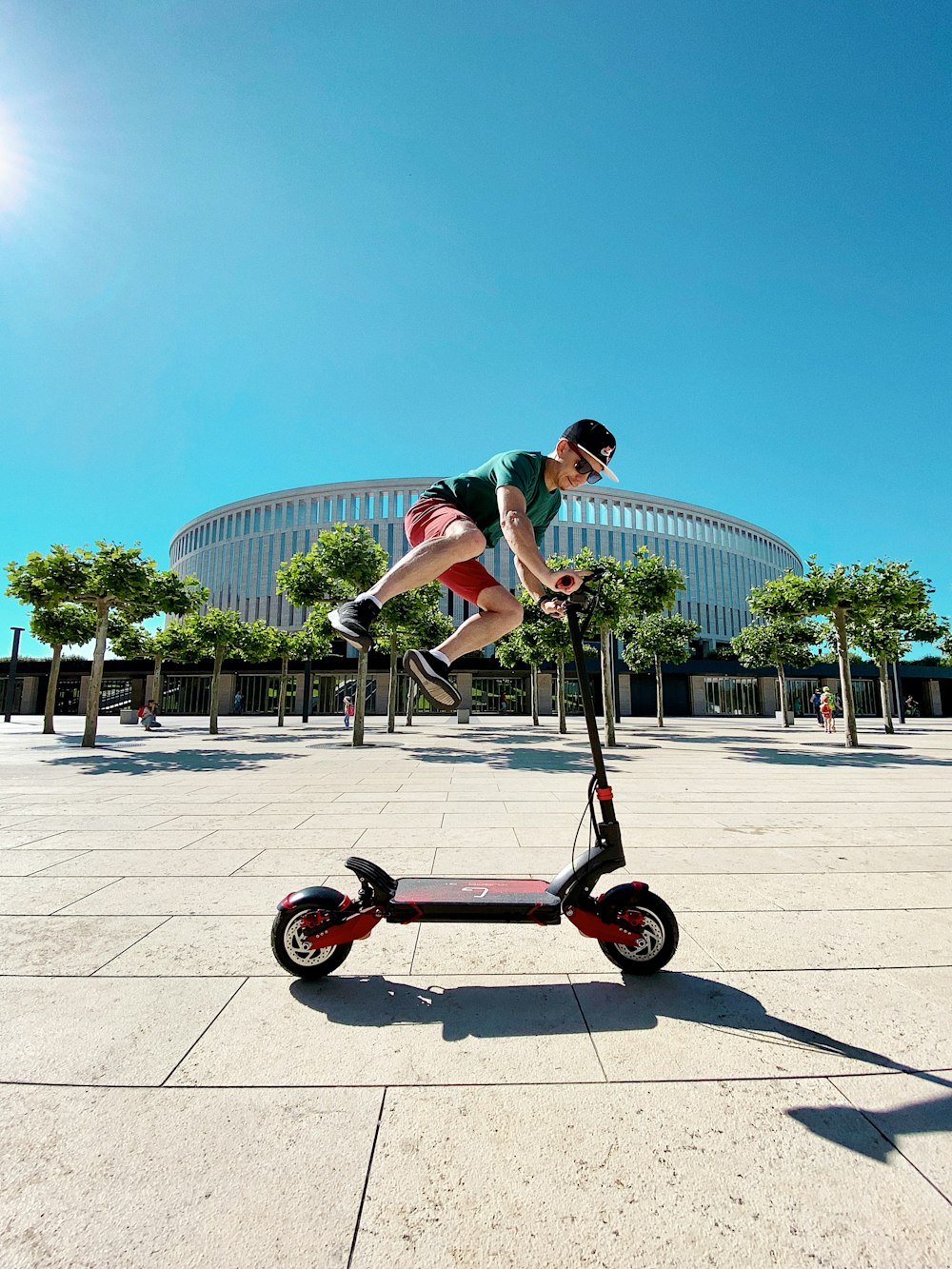 man in green t-shirt and black shorts riding black and red trike during daytime