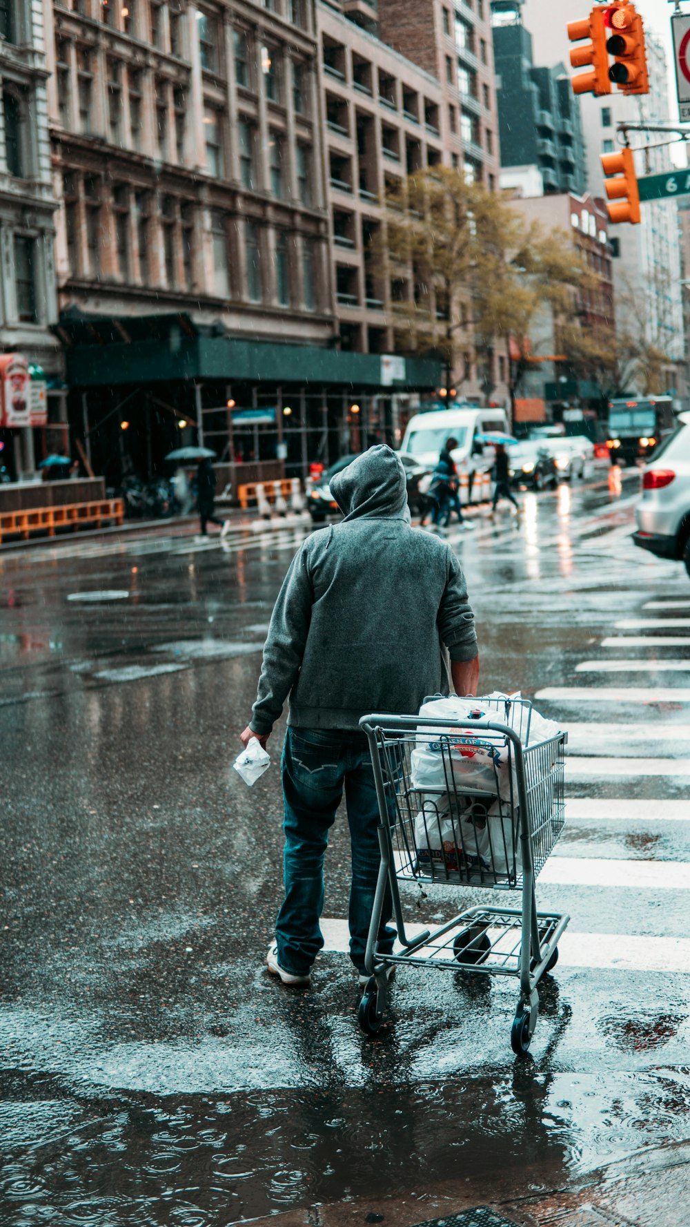 man in gray coat and black pants holding shopping cart on street during daytime