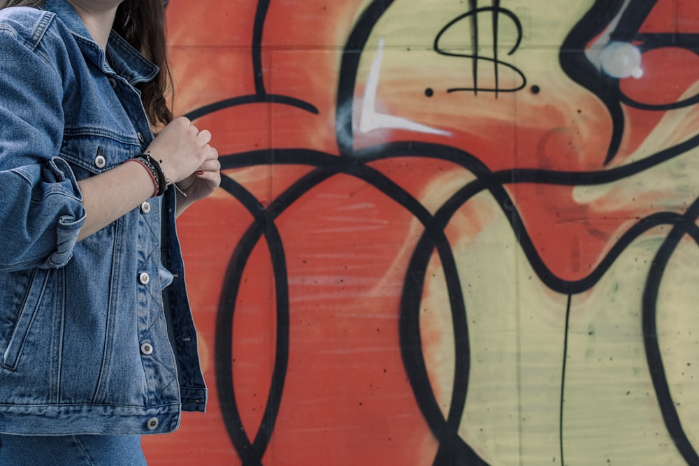 woman in blue denim jacket standing beside wall with graffiti