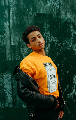 Model wearing off-white tee with bold headline text, standing against a muted charcoal wall.