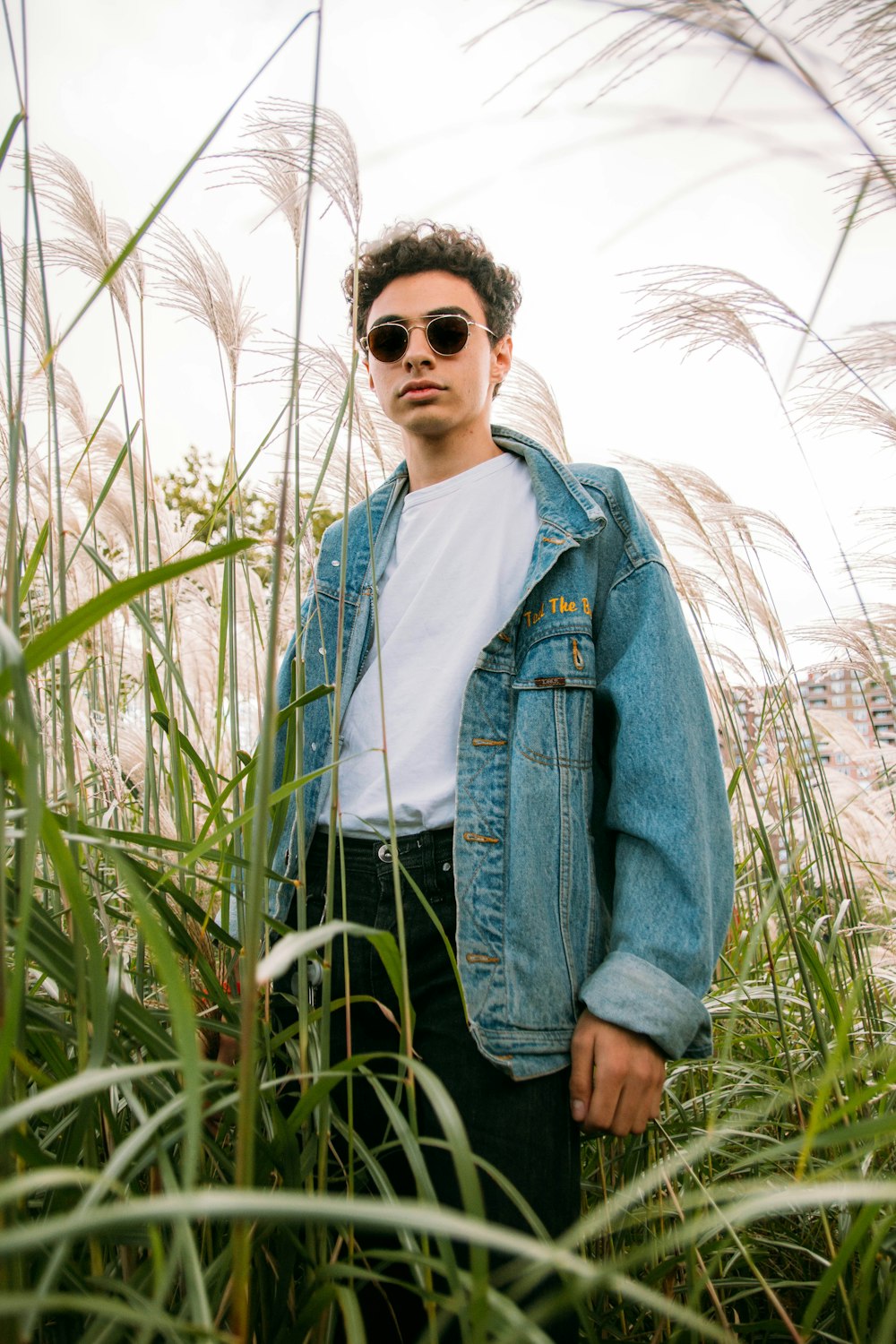 man in blue denim jacket and white shirt standing on green grass field during daytime