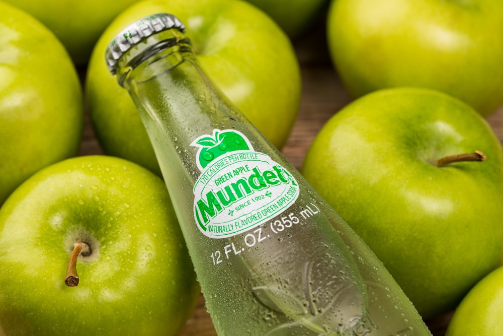 a close up of a bottle of water with apples in the background