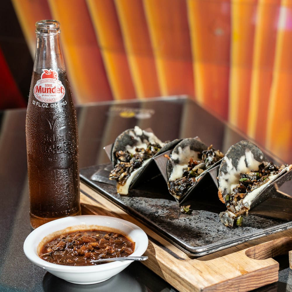 coca cola bottle beside white ceramic bowl with food on brown wooden tray