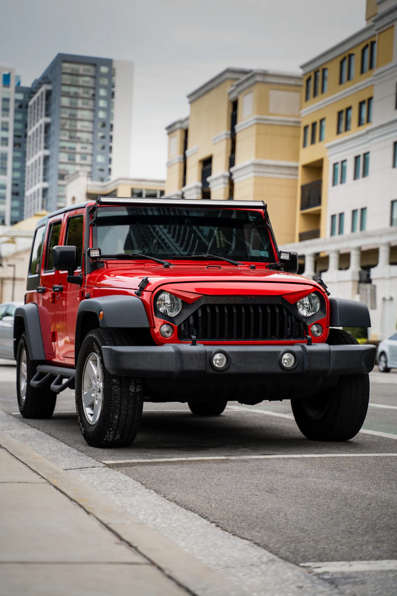 Red 2018 Jeep Wrangler Unlimited Sport with an LED light bar parked at a city curb