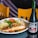 A plate of food containing a grilled piece of fish topped with olives, celery, and assorted vegetables, accompanied by mashed potatoes and rice. A salad with lettuce and a slice of tomato is also on the plate. Next to the plate, there is a bottle of Sangría Señorial, a non-alcoholic beverage. Two wooden chairs are in the background.