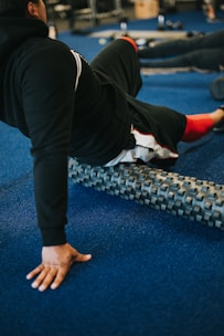 person in black pants and shirt using a foam roller