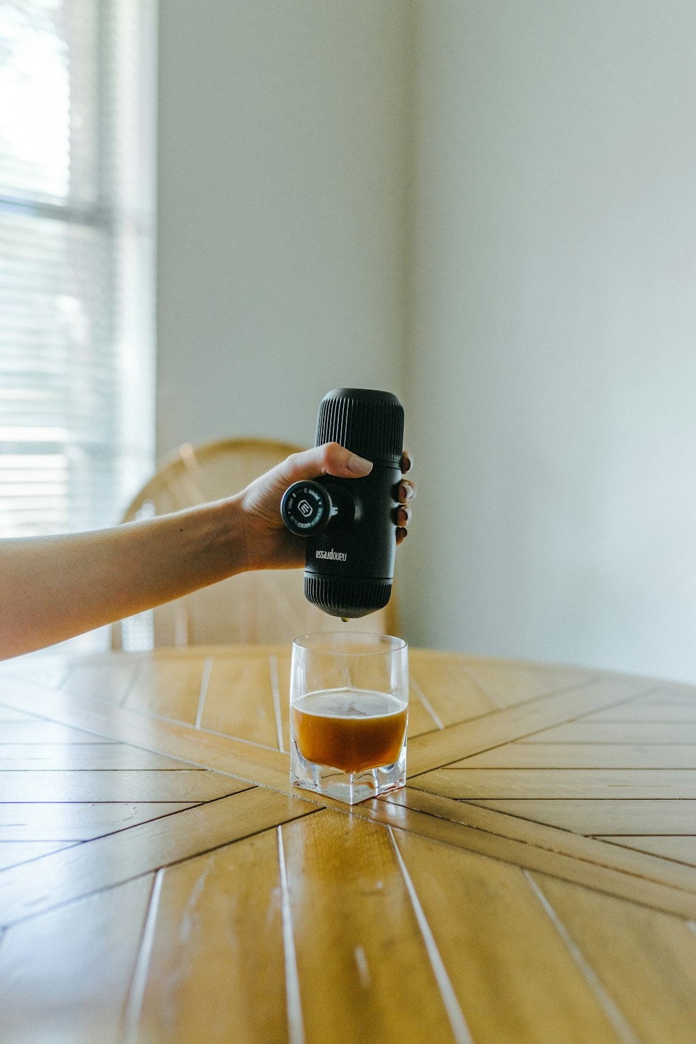 person pouring brown liquid on clear drinking glass