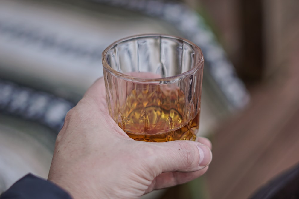 person holding clear shot glass with brown liquid