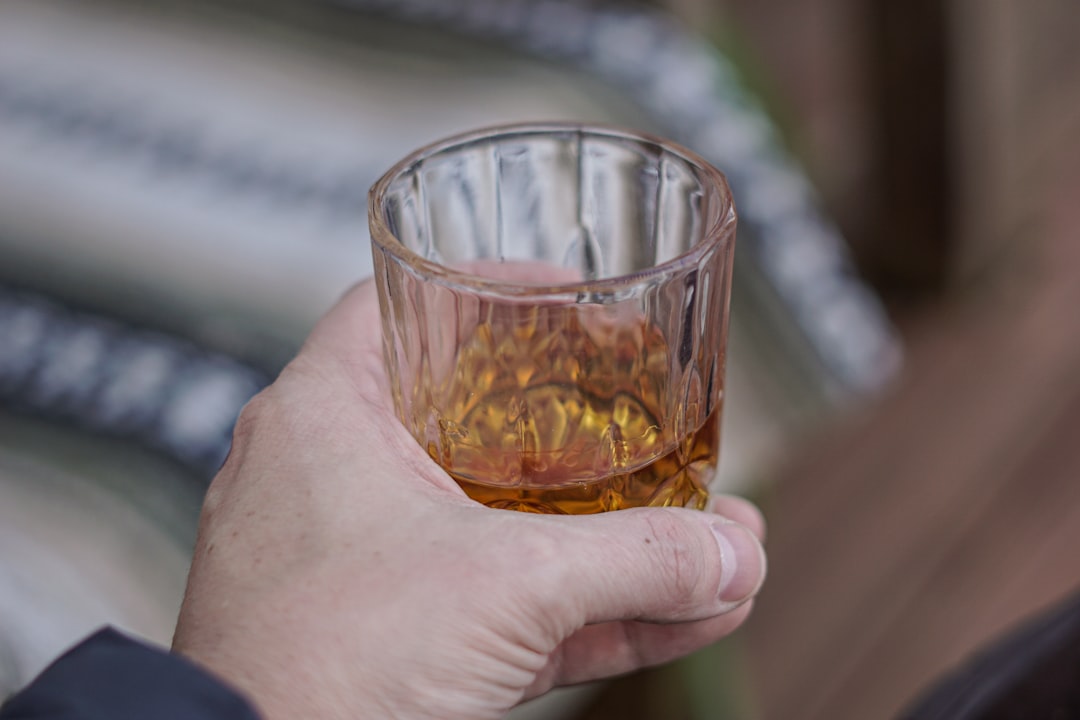 Man's hand gripping a glass of bourbon. 