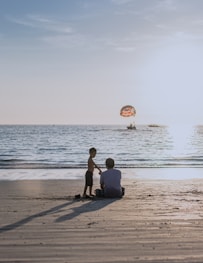 2 men sitting on beach shore during daytime