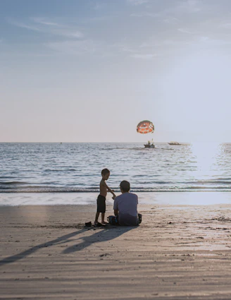 2 men sitting on beach shore during daytime