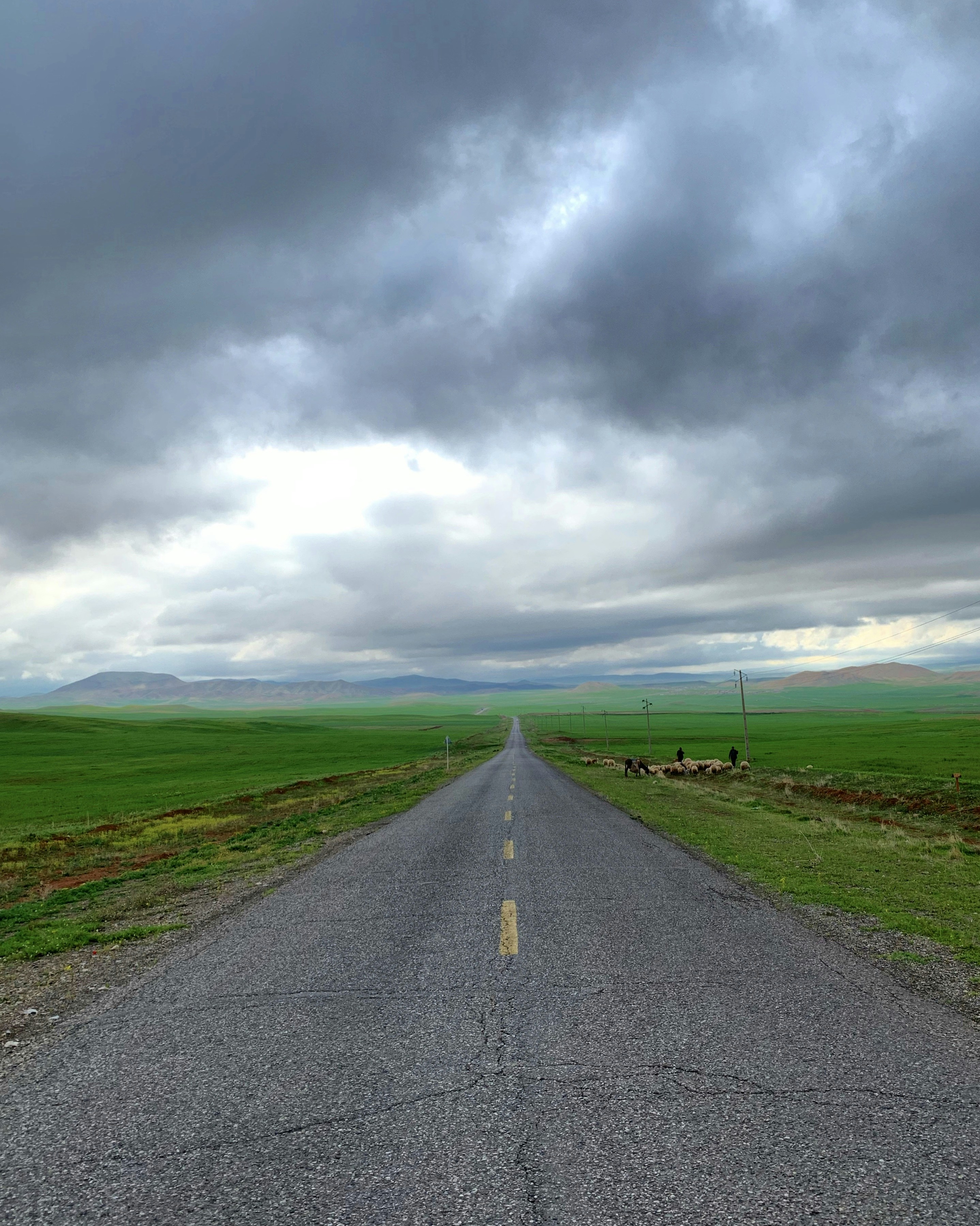 route goudronnée grise entre un champ d’herbe verte sous un ciel nuageux gris pendant la journée