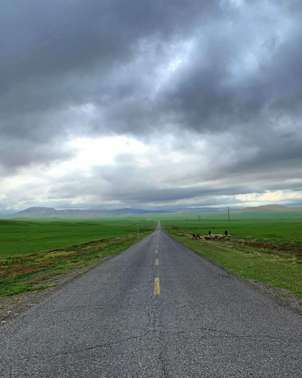 estrada de asfalto cinza entre campo de grama verde sob céu nublado cinza durante o dia