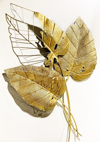 Artistic metal wall art piece featuring nature-inspired shapes with aged patina, casting subtle shadows on a clean wall.