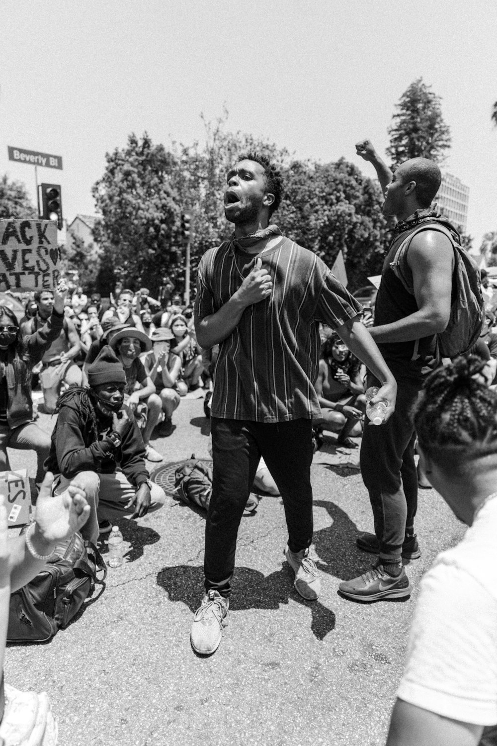 grayscale photo of man in tank top and pants standing on road