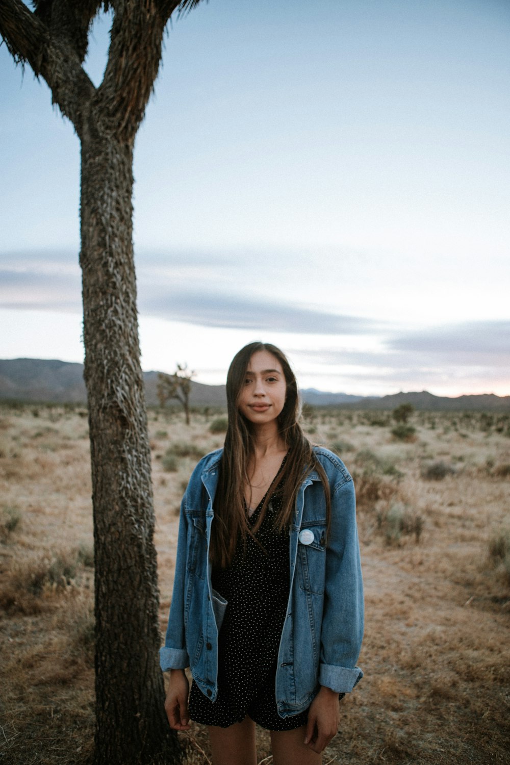 woman in blue denim jacket standing beside brown tree during daytime