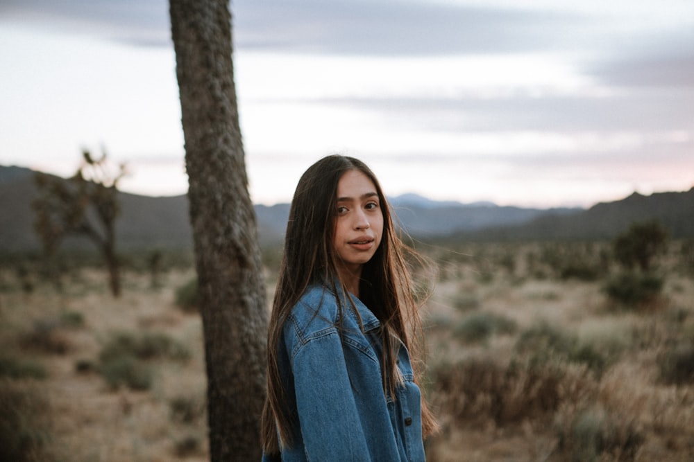 woman in blue denim jacket standing near brown tree during daytime