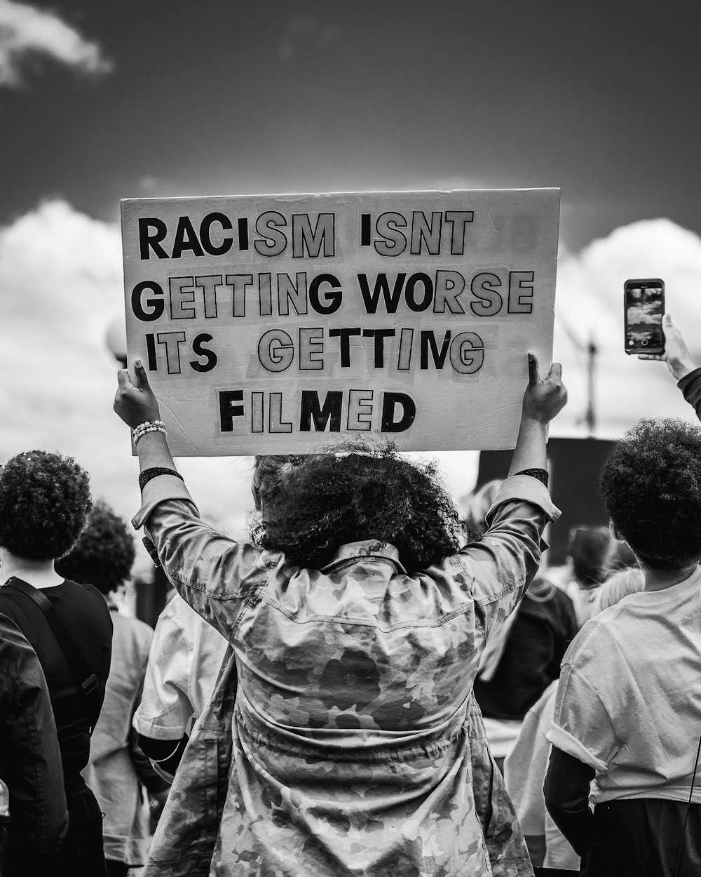 a woman holding a sign that says racism isn't getting worse it's