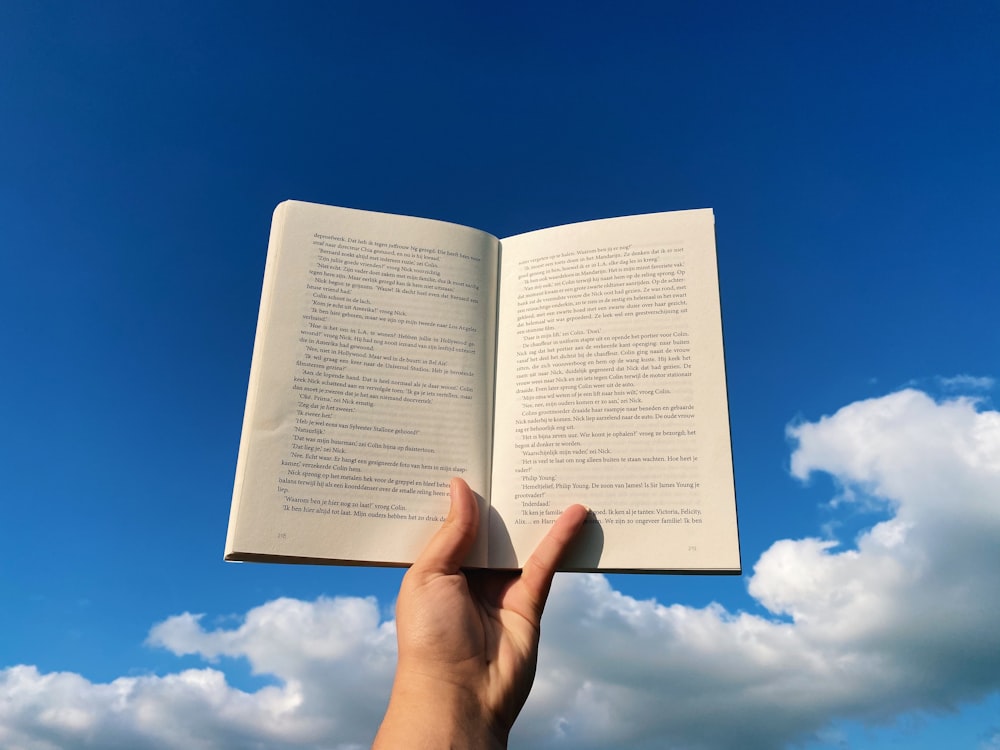 Persona che tiene la pagina del libro bianco sotto il cielo blu durante il giorno