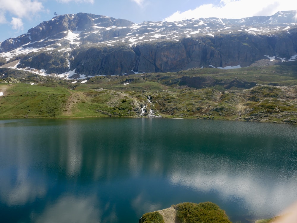 L'erba verde e la montagna coperta di neve bianca accanto al lago durante il giorno