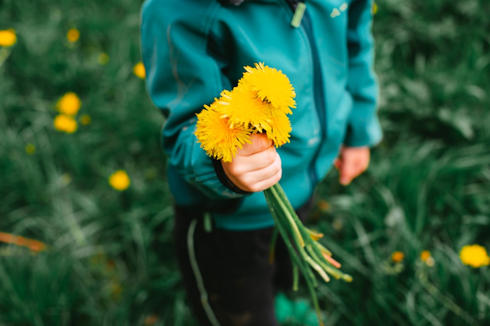 person in blue jacket holding yellow flower